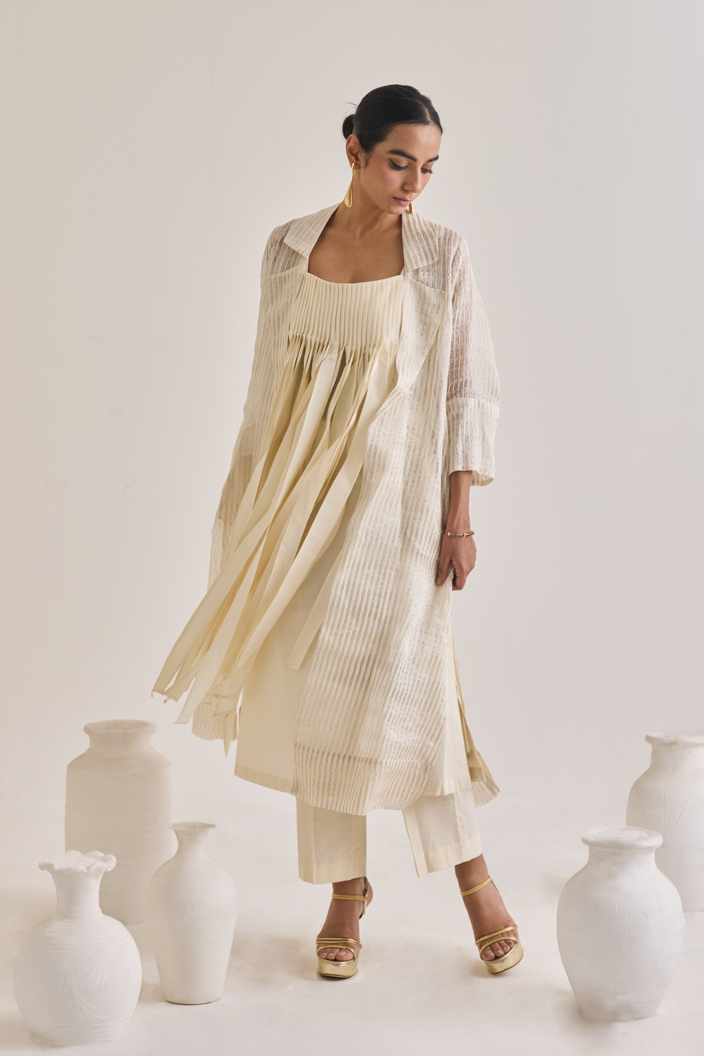Front view of a off white Cotton fringed set with a Long coat having notched collar, Sleeveless cotton Kurta with Front fringes and crease pants.