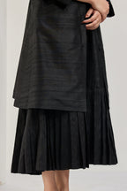 Close-up of the pleated hem on a black raw silk midi dress
