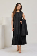 Model in black raw silk sleeveless midi dress with round neckline and pleated hem, without coat, front view