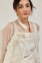 Model seated on a chair in a white Chanderi co-ord set with sheer organza jacket