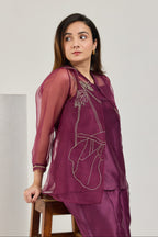 Seated view of wine Chanderi top, organza jacket and straight pants with organza at the leg opening