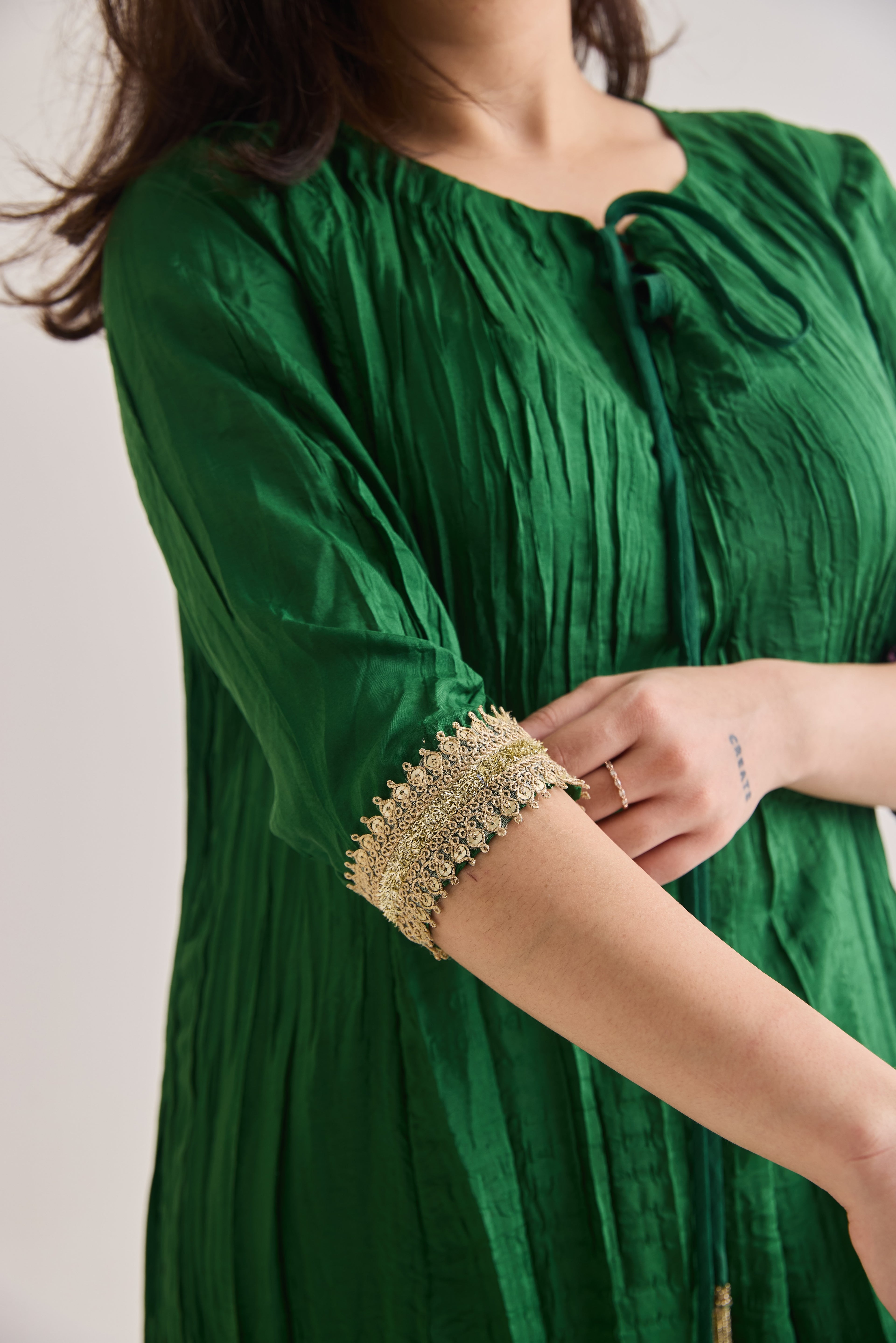 Close up shot of a Green suit with 3/4th sleeves and a tie up neck made out of crushed silk fabric with Golden gota detail on sleeve