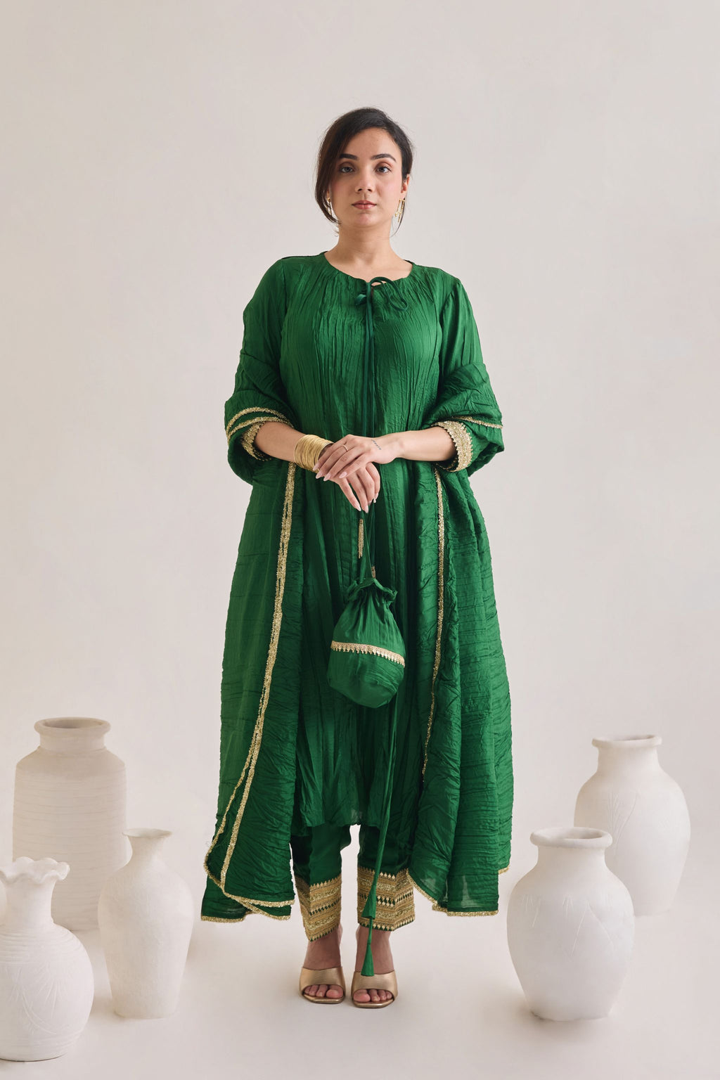 Green suit with 3/4th sleeves and a tie up neck with salwar made out of crushed silk fabric with Golden gota detail and accessorized with a Drawstring Bag