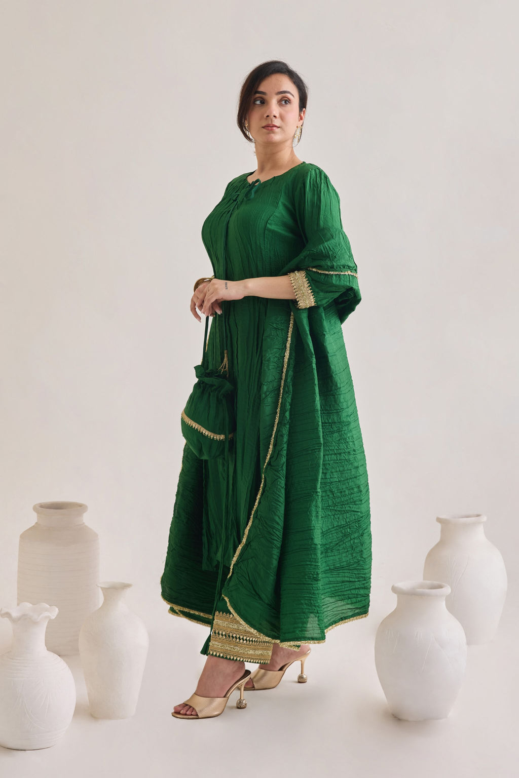Side profile of a Green suit with 3/4th sleeves and a tie up neck with salwar made out of crushed silk fabric with Golden gota detail and accessorized with a Drawstring Bag and a silk and lace dupatta 