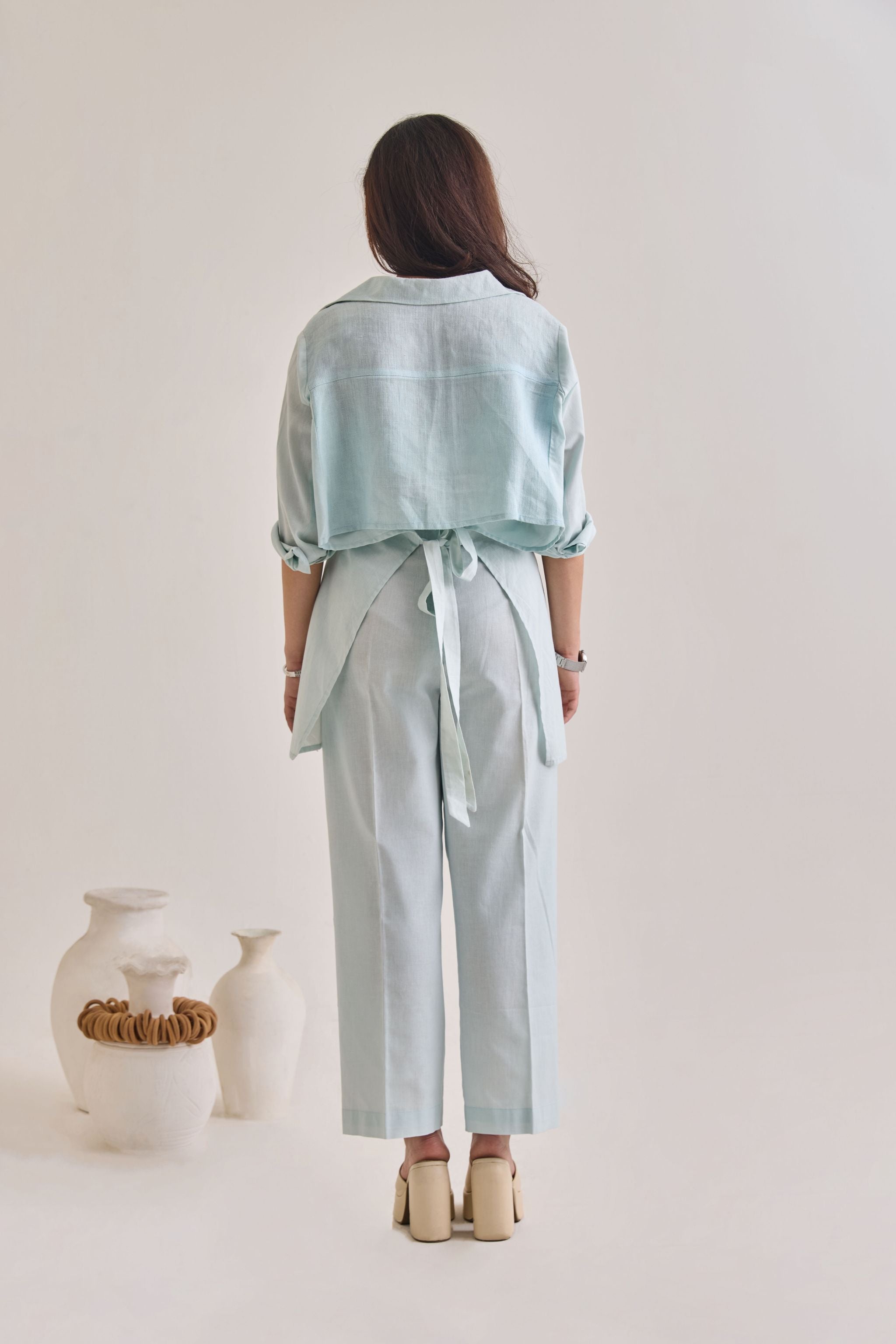 Back view of Pastel Blue Cotton-Linen Shirt with Sleeves rolled up and back tied with a knot to make it look elevated.