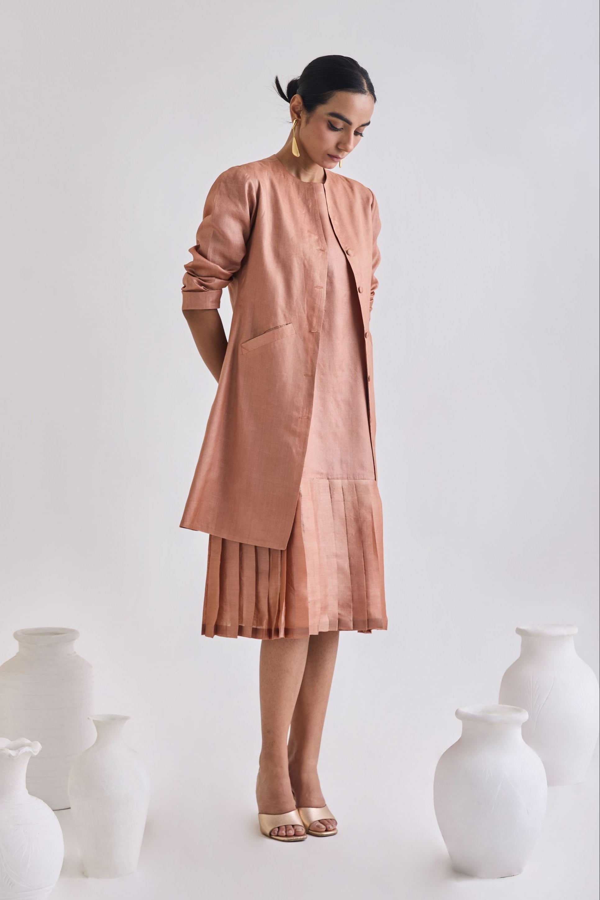 Front view of sleeveless pleated dress with Full sleeve tussar coat with slant pockets and full sleeve rolled up to elbow