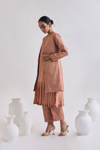 Side view of Pure tussar set with a pleated sleeveless dress, a coat which has long sleeves and slant pockets, and a pair of tailored pants.