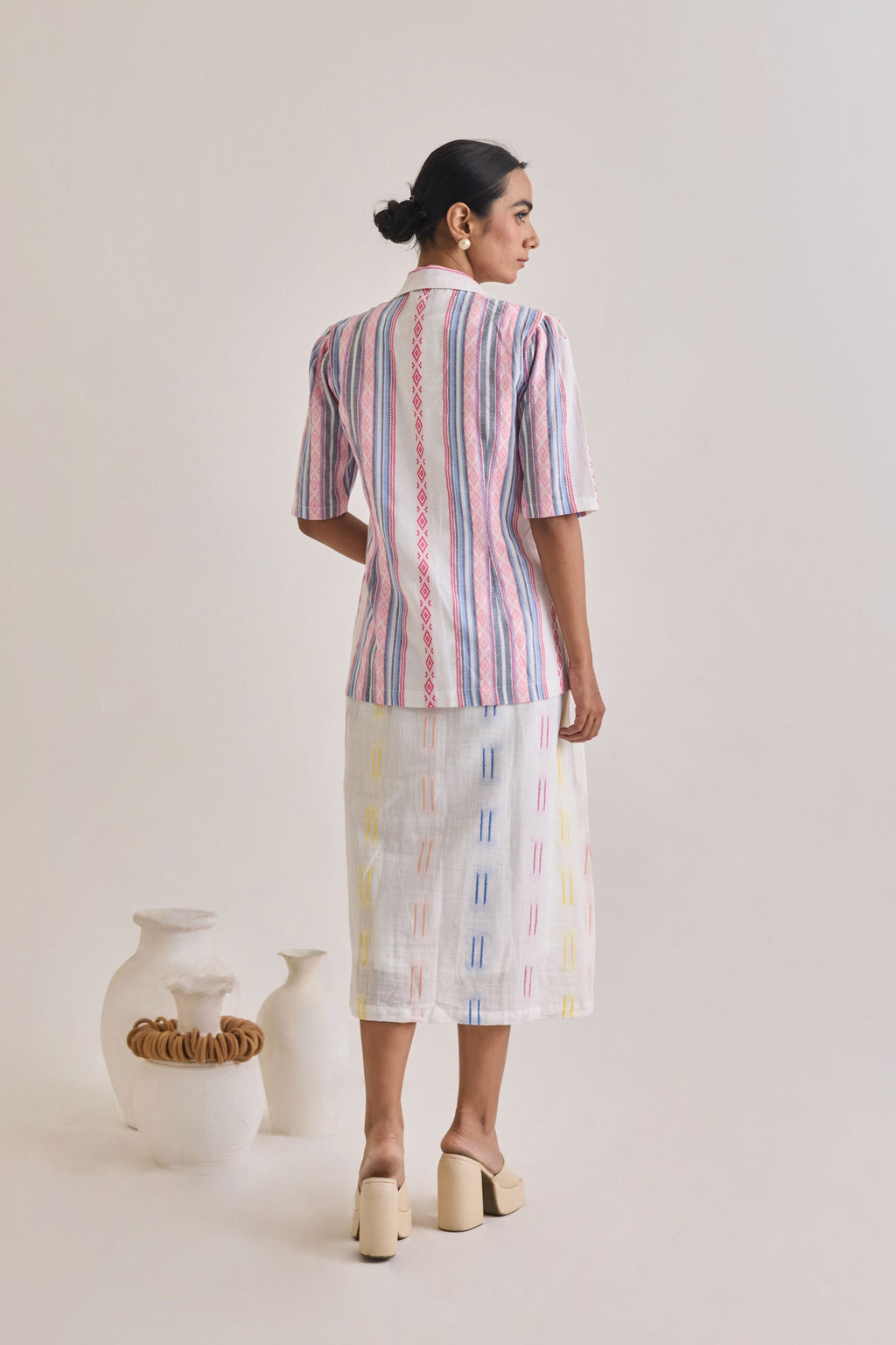 Back profile of a white cotton dress with weaved multi color design and a blazer with elbow length sleeves with pink and blue stripes woven to the fabric