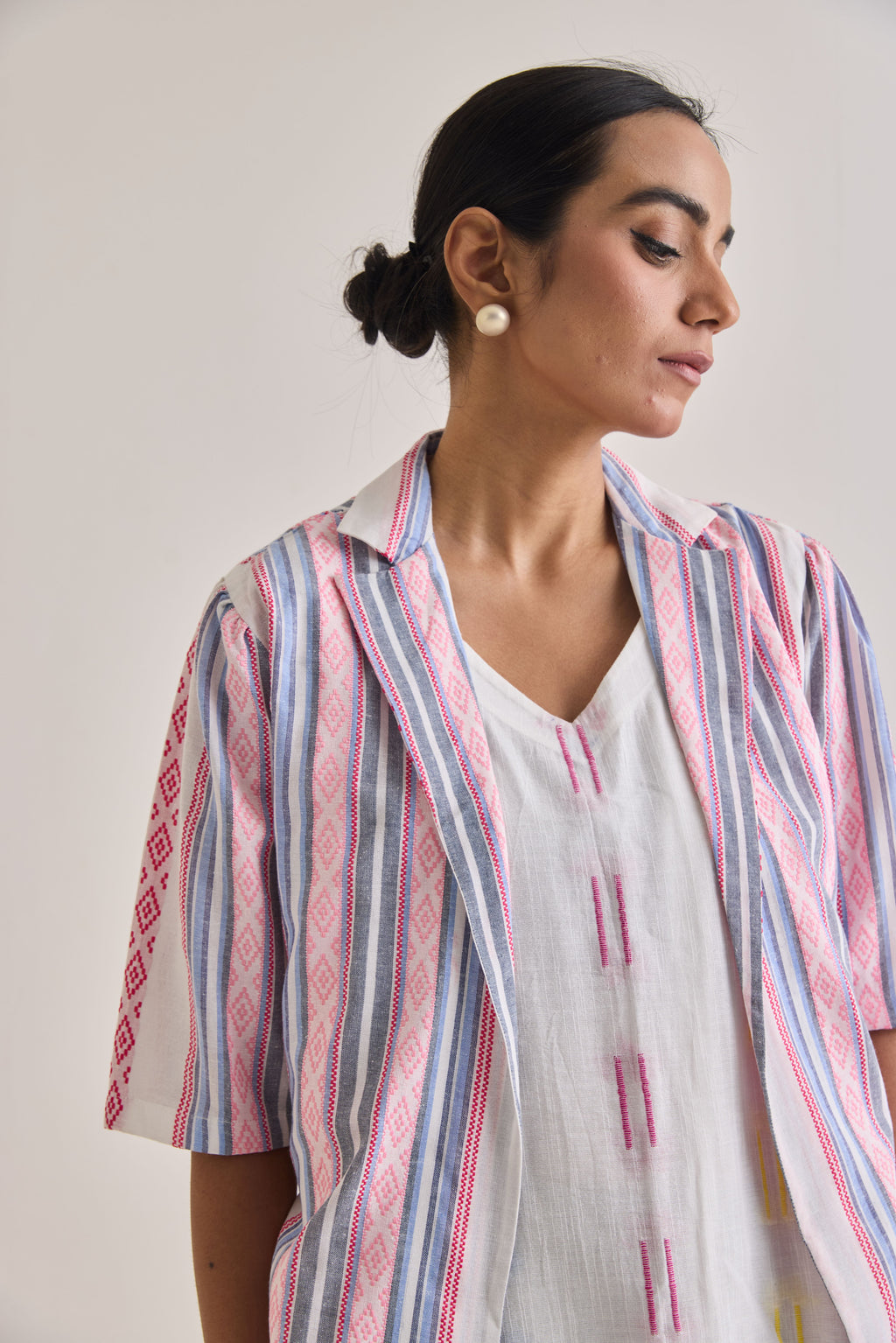 Front close up profile of a white cotton dress with weaved multi color design and a blazer with elbow length sleeves with pink and blue stripes woven to the fabric