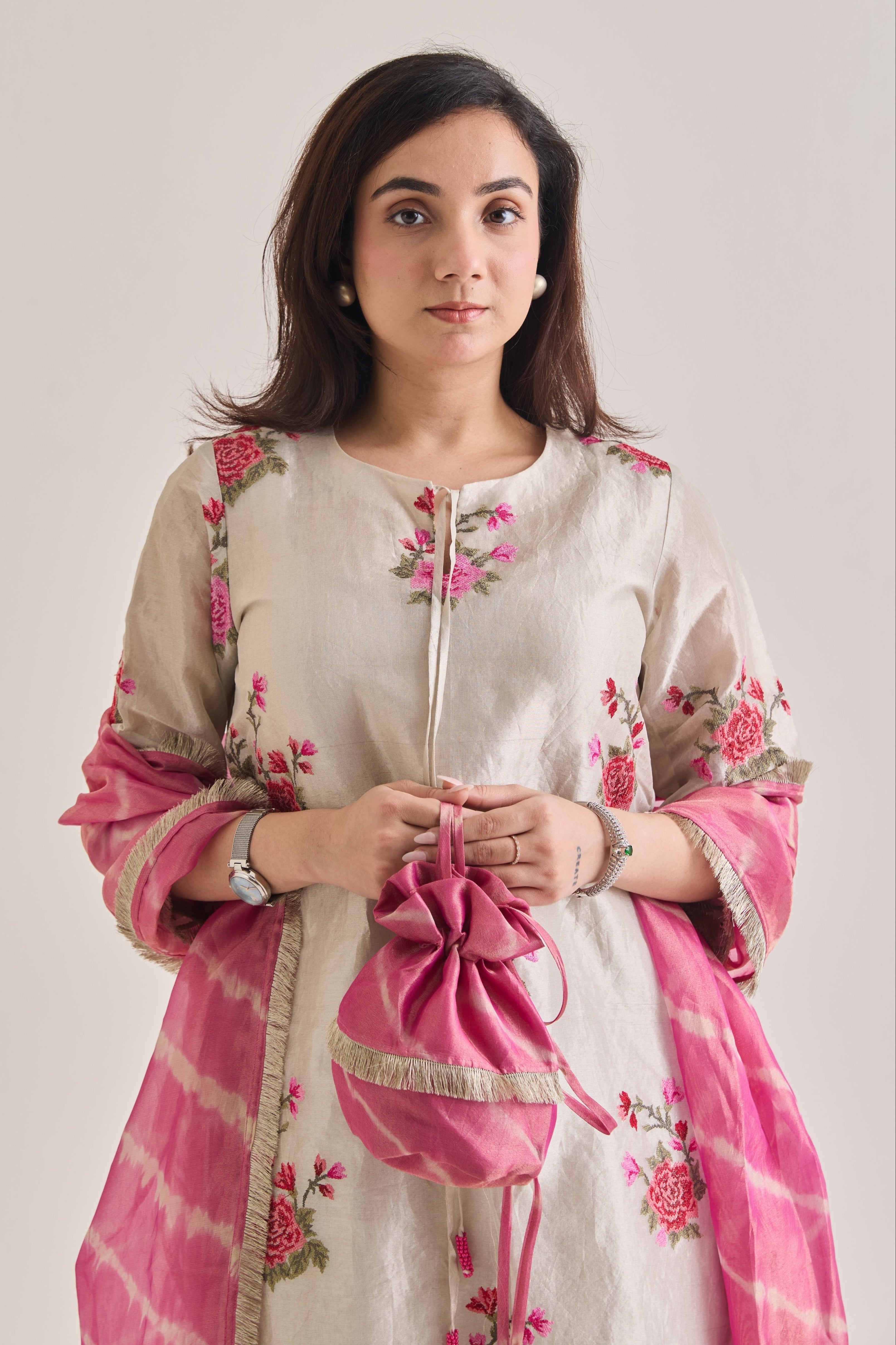 Close up detail shot of Silver and pink Farsi suit salwar set made out of Silver tissue with a machine embroidered rose motif kameez having 3/4th sleeves and tie neck detail, and Pink organza laheriya print dupatta paired with a Potli Bag.