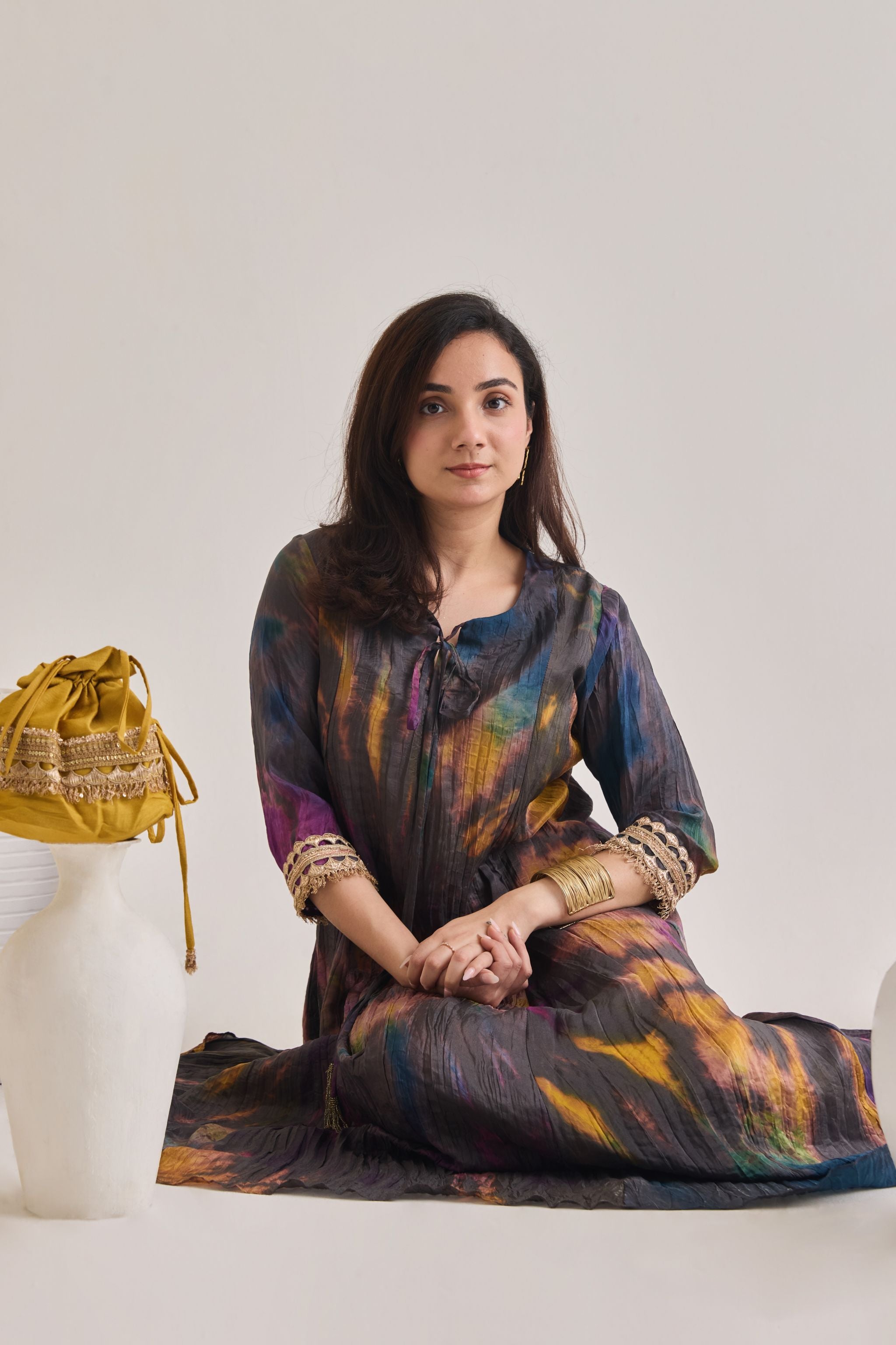 Close up view of multicolour suit made out out of crushed silk fabric with 3/4th length sleeves having gota border at sleeve opening and Dori neckline, accessorized with a mustard gota Drawstring bag.