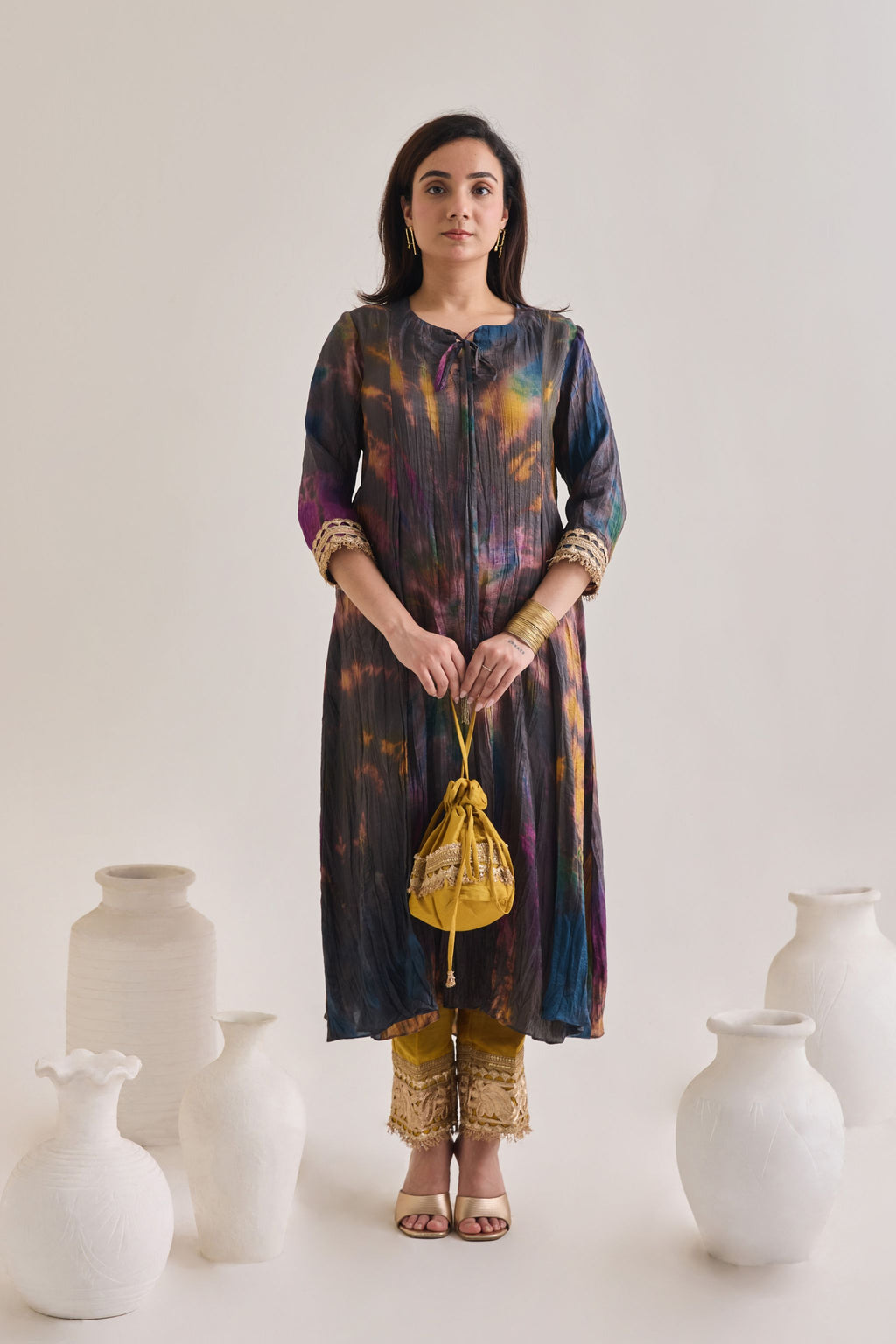 Front profile of multicolour suit made out out of crushed silk fabric with 3/4th length sleeves having gota border at sleeve opening and Dori neckline, paired with a pair of mustard salwar with golden gota and a mustard gota Drawstring bag.