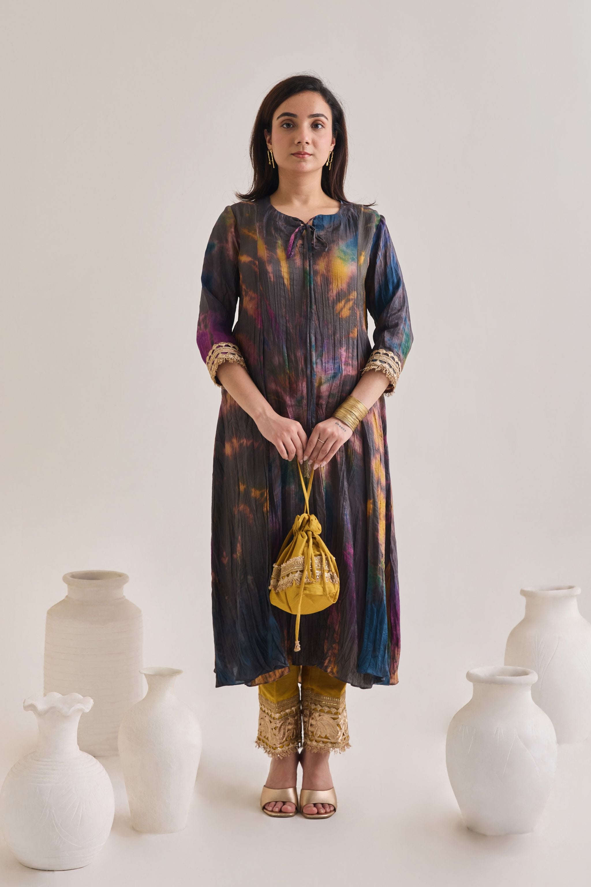 Front profile of multicolour suit made out out of crushed silk fabric with 3/4th length sleeves having gota border at sleeve opening and Dori neckline, paired with a pair of mustard salwar with golden gota and a mustard gota Drawstring bag.